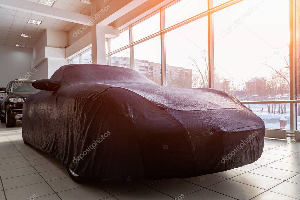 A prepared gift at a car dealership, a sports car closed with a blue case made of special fabric, sewn in an individual workshop that fits all smooth body lines.
