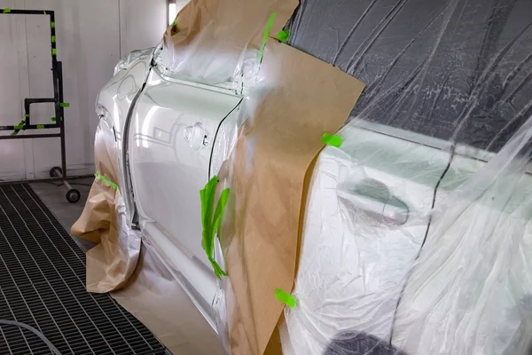 Painting the white door of the car SUV in the workshop for body repair. Car covered with paper and envelop from hitting paint.