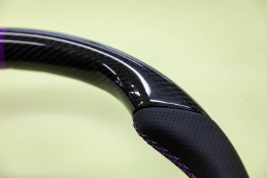 Siyah karbon fiber delikli deri ile yapılmış bir direksiyon simidi detay Close-up bir tasarım ve otomobil yedek parçalar için ayarlama atölye mor iplik ile dikişli.