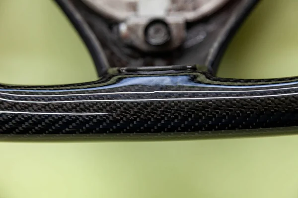 The lower part of the steering wheel of a carbon fiber vehicle is a close-up of black color on the assembly of spare parts and equipment in a car tuning workshop.