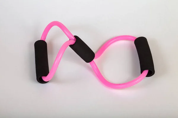 Pink rubber tube expander with black paralon handles for performing fitness exercises with hands in the form of an infinity sign on a white isolated background