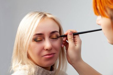 Oryantal tarzda modelinde salonda makyaj uygulayarak, yakın çekim, yüzyılın bir fırçayla köşelerinde altın kahverengi tonları ve yeşil koyarak makyöz elinde tuttu..