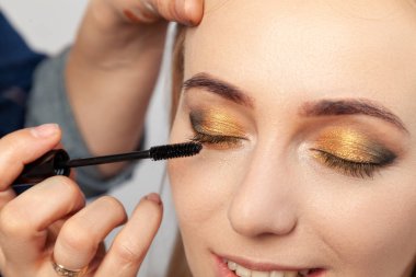 Yakın çekim bir oryantal tarzı göz makyaj: altın, kahverengi ve yeşil belirgin göz gölgeler, makyaj sanatçısı bir fırça elinde tutuyor ve maskara ile modeli kirpik boyaları.