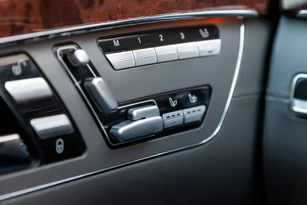 Automatic seat memory buttons with white signs and symbols located diagonally from top to bottom on a grey modern car control panel with brown and chrome-plated metal elements.