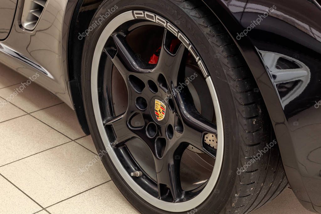 Novosibirsk, Russia - 08.01.2018: A cast disc in black with a white rim and a brand sign in the form of a coat of arms in the center for a Porsche Boxter with perforated brakes in close-up.