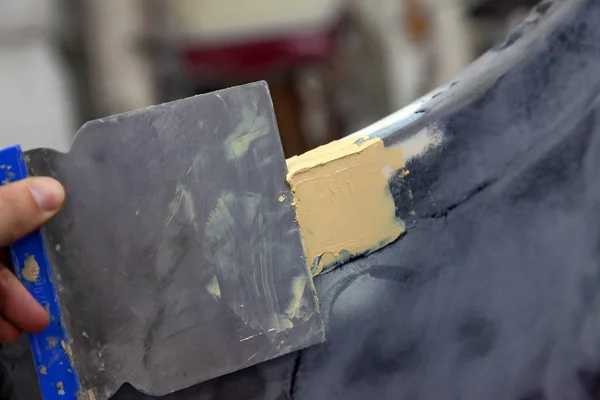 The master at work in a car workshop applies a putty with a coating to grout a coating bumper on a damaged element of the car body and prepares it for further painting.