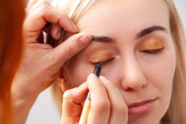 Oryantal tarzda modelinde salonda makyaj uygulayarak, yakın çekim, elinde düzenlenen bir fırça ile altın kahverengi tonları ve yeşil köşe yüzyılın makyaj sanatçısı yüklemektedir. 