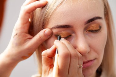 Makyöz bir elinde bir kalem yardımı ile bir ok model gözünü çizer, diğer elini de makyaj daha iyi 