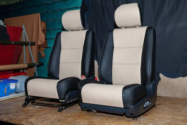 Two front seats with combined leather trim in two colors of black and beige, located on the workbench in the workshop for repair and tuning of cars and vehicles