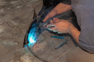 Deneyimli bir kişi bir kaynak makinası ile metal parçalar, mavi duman çıkarmadan sabitleme gerçekleştiren ve sarı kıvılcım ve endüstriyel üretim atölyesinde yıldırım.