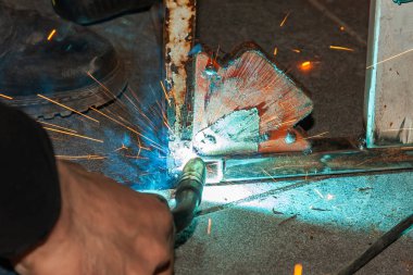 Deneyimli bir kişi bir kaynak makinası ile metal parçalar, mavi duman çıkarmadan sabitleme gerçekleştiren ve sarı kıvılcım ve endüstriyel üretim atölyesinde yıldırım.