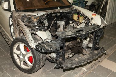Atölye demonte beyaz araba tamir için hazırlanan: ön uç, kaput ve tampon iç donanımları, kaldırıldı ve yedek parçalar motor görünür.
