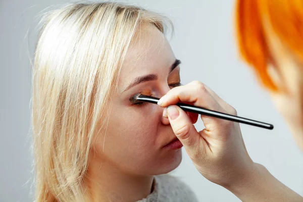 Visagiste med en børste i den ene hånd at sætte makeup på øjnene af - Stock-foto