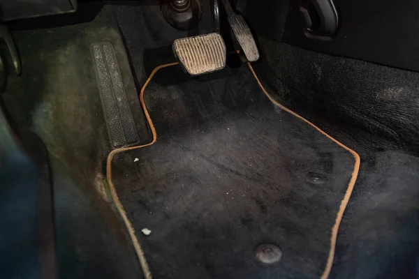 Dirty car floor mats of black carpet with gas pedals and brakes