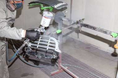 Bir erkek işçi boya tabancası ile araba vücut parçası boyar. 