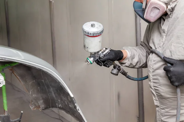 A male worker paints with a spray gun a part of the car body in