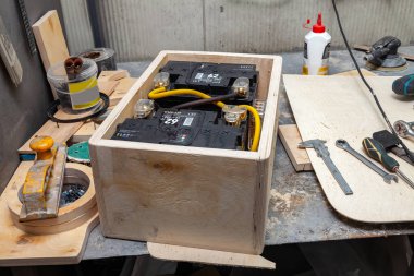 Wooden box with two car batteries connected together on a workbe clipart