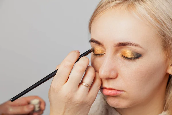 Visagiste med en børste i den ene hånd at sætte makeup på øjnene af - Stock-foto