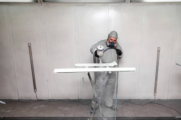 Рабочий мужчина рисует спреем часть кузова машины в
 