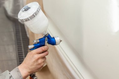 Bir erkek işçi boya tabancası ile araba vücut parçası boyar. 