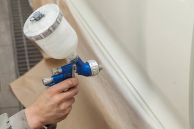 Bir erkek işçi boya tabancası ile araba vücut parçası boyar. 