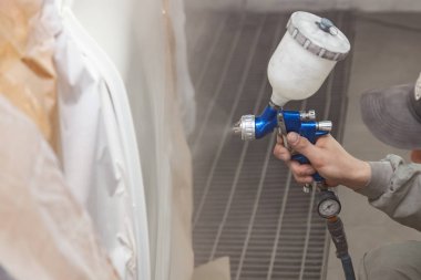 Bir erkek işçi boya tabancası ile araba vücut parçası boyar. 