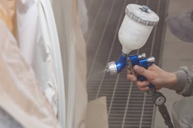 Bir erkek işçi boya tabancası ile araba vücut parçası boyar. 