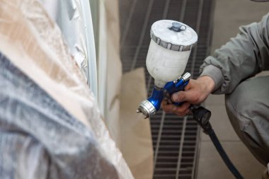 Bir erkek işçi boya tabancası ile araba vücut parçası boyar. 
