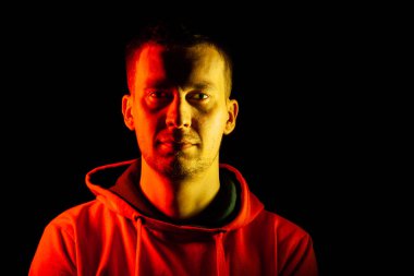 Yetişkin bir adam turuncu kapüşonlu sweatshirt ileriye bakmak duruyor 