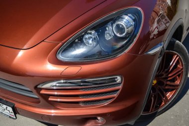 Novosibirsk, Rusya - 05.29.2019: Arka planda gri duvarlı güneşli bir yaz gününde satıştan önce temizlik yaptıktan sonra Porsche Cayenne 958 2013'ün ön ksinion farı, drl ve tekerlek görünümü kahverengi renkte