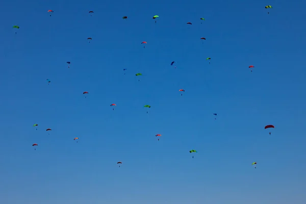 Muchos pequeños paracaidistas en el cielo azul claro con multicolor — Foto de Stock