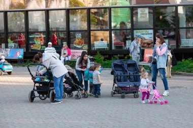 Young mom girls with strollers and small children are walking in