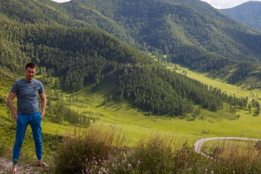 Yeşil tişörtlü adam uçurumun kenarında duruyor. 