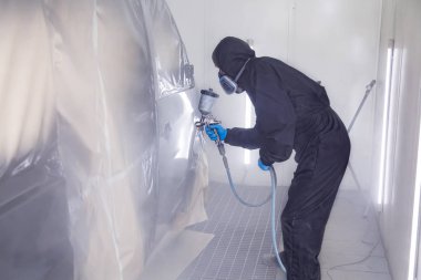 A male worker in jumpsuit and blue gloves paints with a spray gu clipart