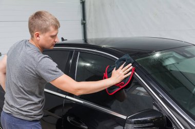 Bir erkek işçi siyah bir araba yıkayan, yumuşak bir bez ile su silerek