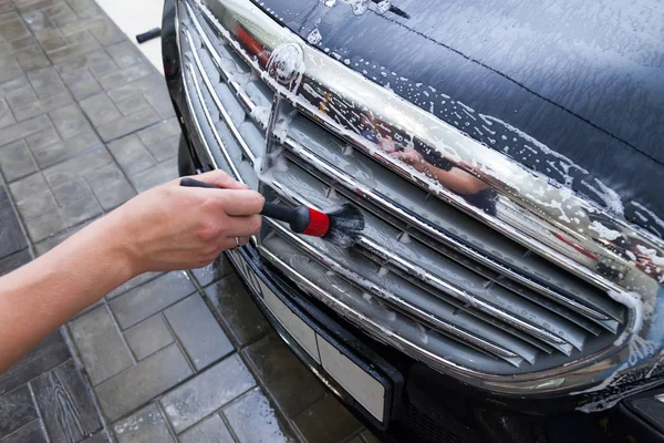 En manlig arbetare tvättar en svart bil med en speciell borste för galler — Stockfoto