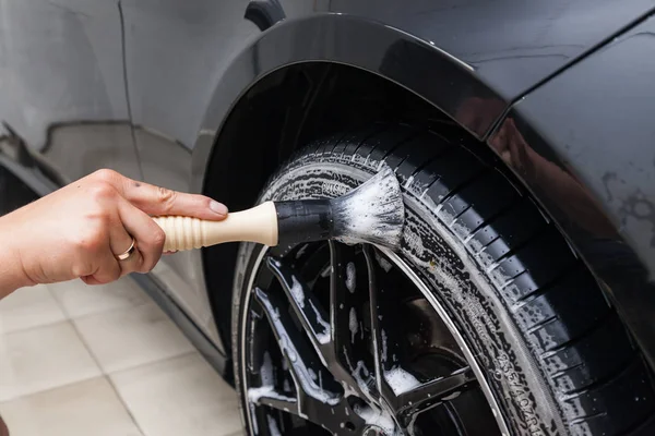 A male worker washes a black car with a special brush for cast w — Stock Photo, Image