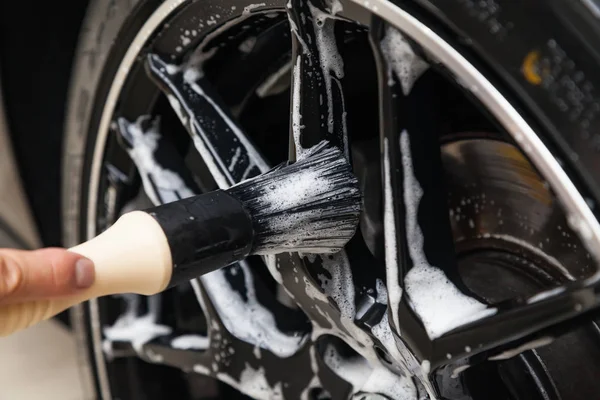 A male worker washes a black car with a special brush for cast w — Stock Photo, Image