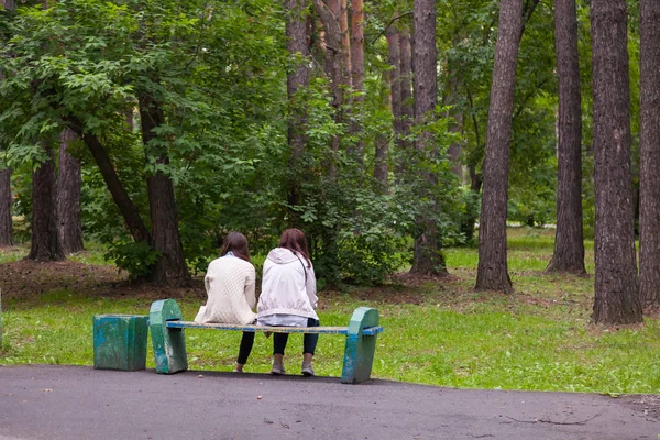 Две девушки сидят на старой деревянной скамейке в городском парке — стоковое фото