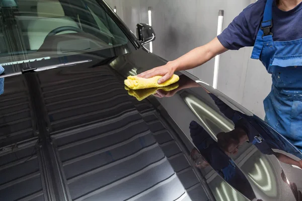 Un operaio in tuta blu pulisce il cofano di una macchina nera — Foto Stock