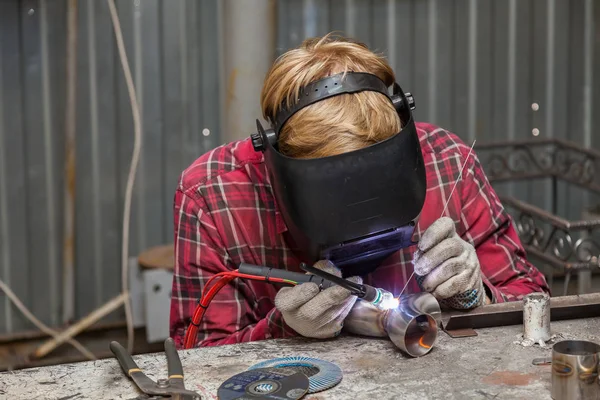 Young guy welder in a checkered red shirt welds a stainless stee