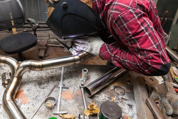 Young guy welder in a checkered red shirt welds a stainless stee