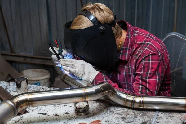 Young guy welder in a checkered red shirt welds a stainless stee