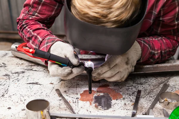 Young guy welder in a checkered red shirt welds a stainless stee — Stock Photo, Image