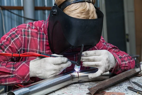 Young guy welder in a checkered red shirt welds a stainless stee