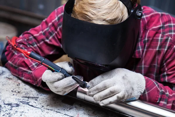 Young guy welder in a checkered red shirt welds a stainless stee