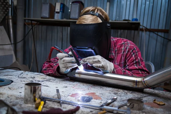 Young guy welder in a checkered red shirt welds a stainless stee