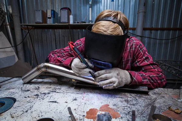 Young guy welder in a checkered red shirt welds a stainless stee