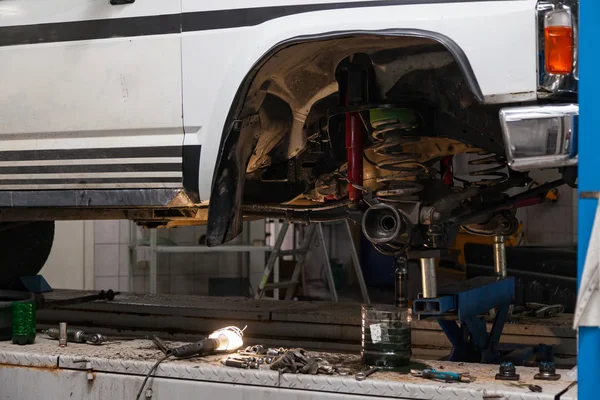 Car suspension repair in the back of a white SUV on a lift with