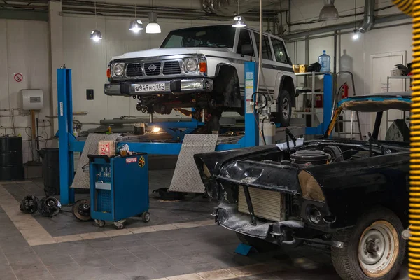 Coche usado blanco Nissan Patrol levantado en un ascensor azul para reparar — Foto de Stock